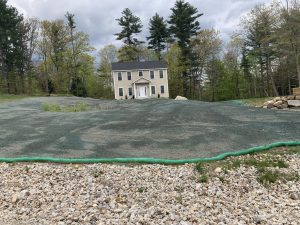 A two-story house with a freshly seeded lawn surrounded by trees and a gravel foreground.