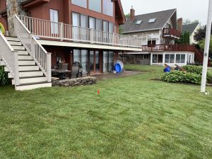 Two-story house with large windows and a wraparound deck, overlooking a lawn with some yard equipment.