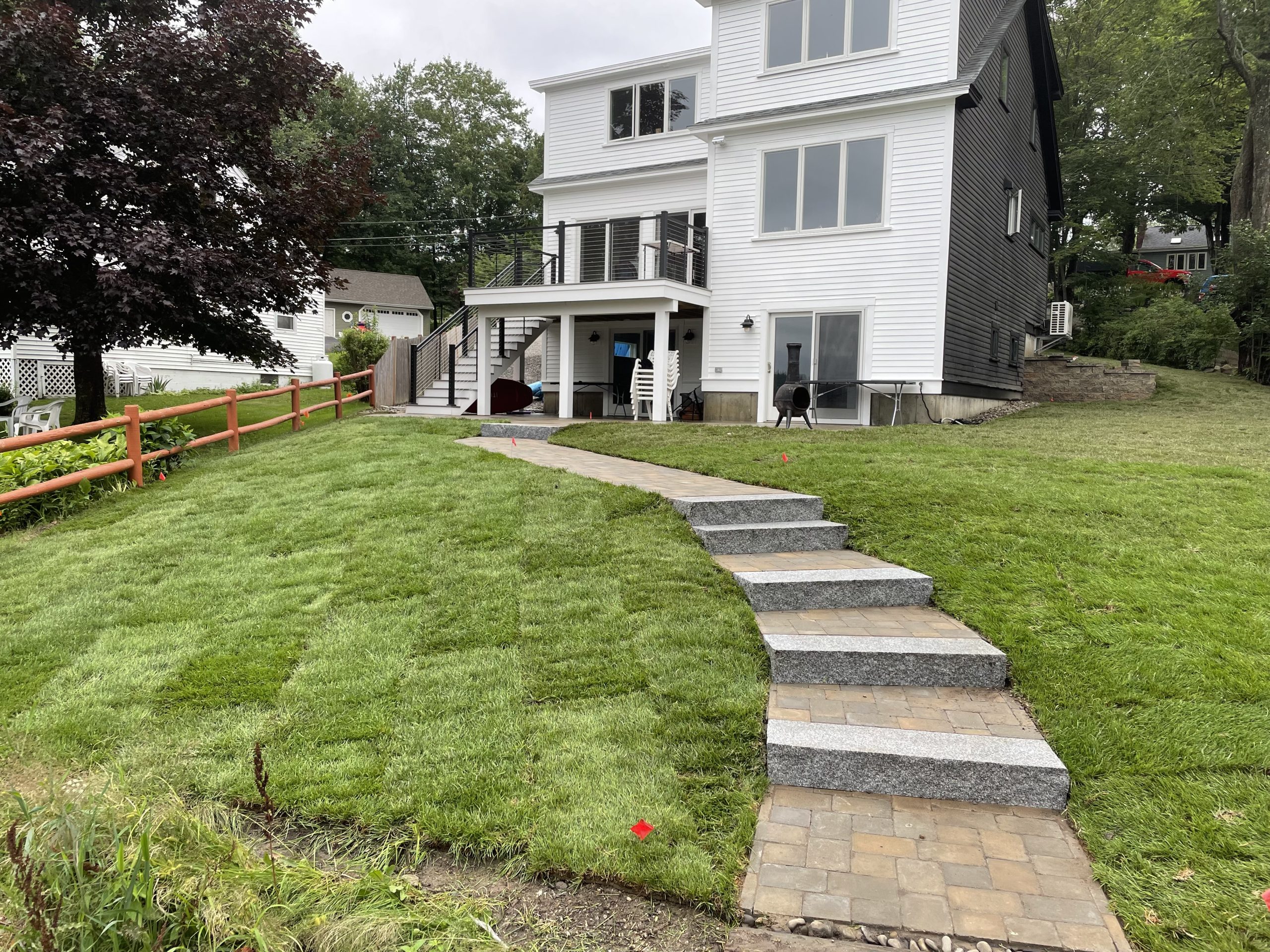 A white multi-story house with a freshly laid sod lawn. A stone pathway with steps leads to the front entry. A wooden fence borders the left side of the yard.