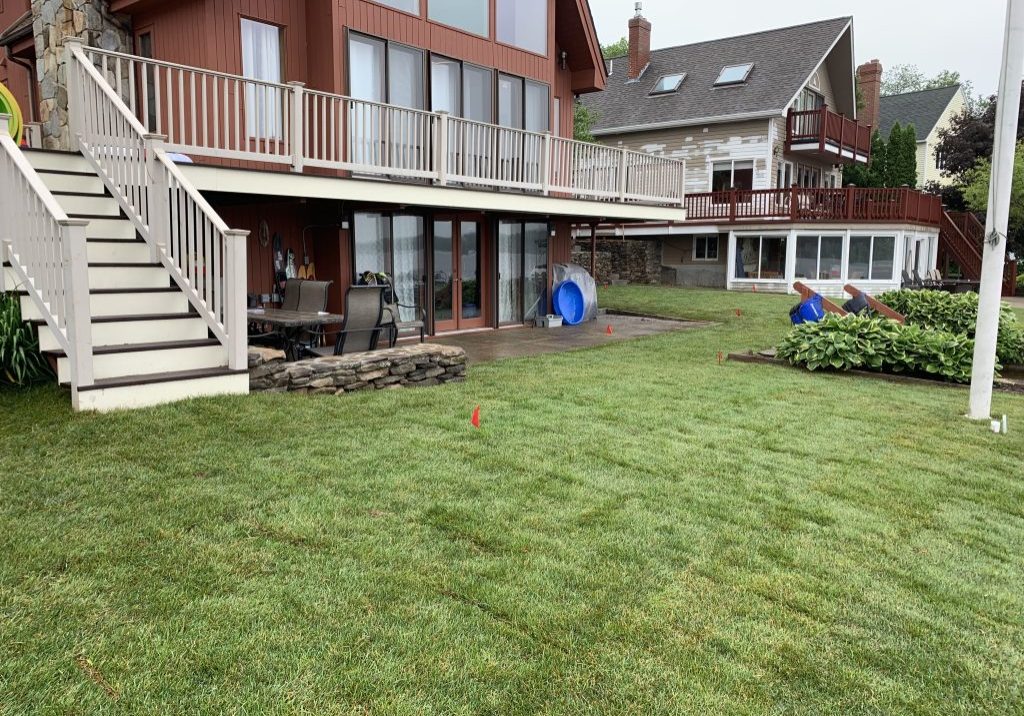 Two-story house with large windows and a wraparound deck, overlooking a lawn with some yard equipment.